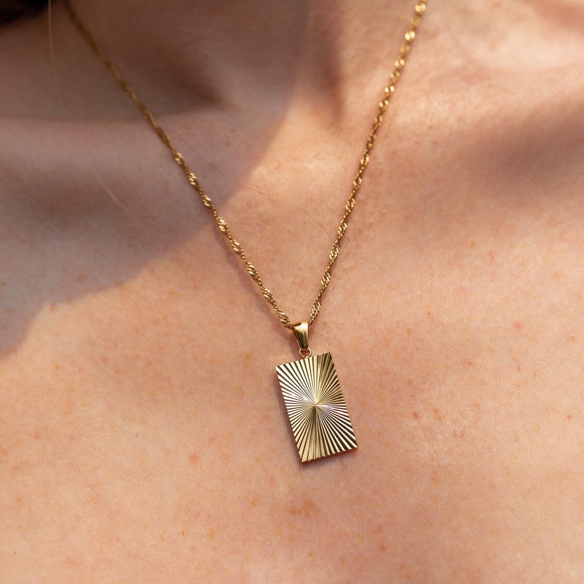 A close-up image of a gold-plated necklace with a lobster clasp and a chain, worn by a person.