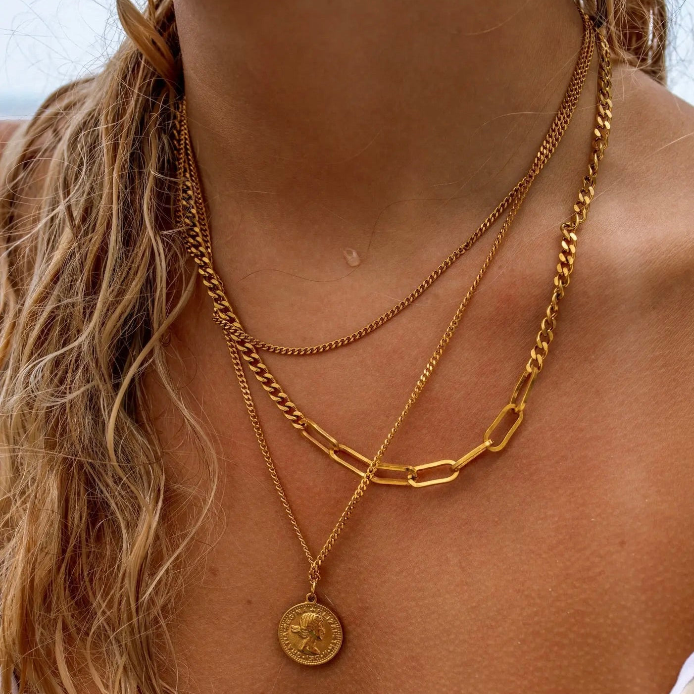 A layered gold necklace with a coin pendant, displayed on a person's neck.