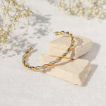 Gold and silver twisted bracelet on a light stone surface with delicate flowers in the background