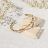 Gold and silver twisted bracelet on a light stone surface with delicate flowers in the background