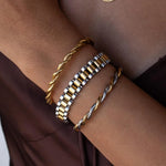 Three gold and silver bracelets on a wrist against a brown background