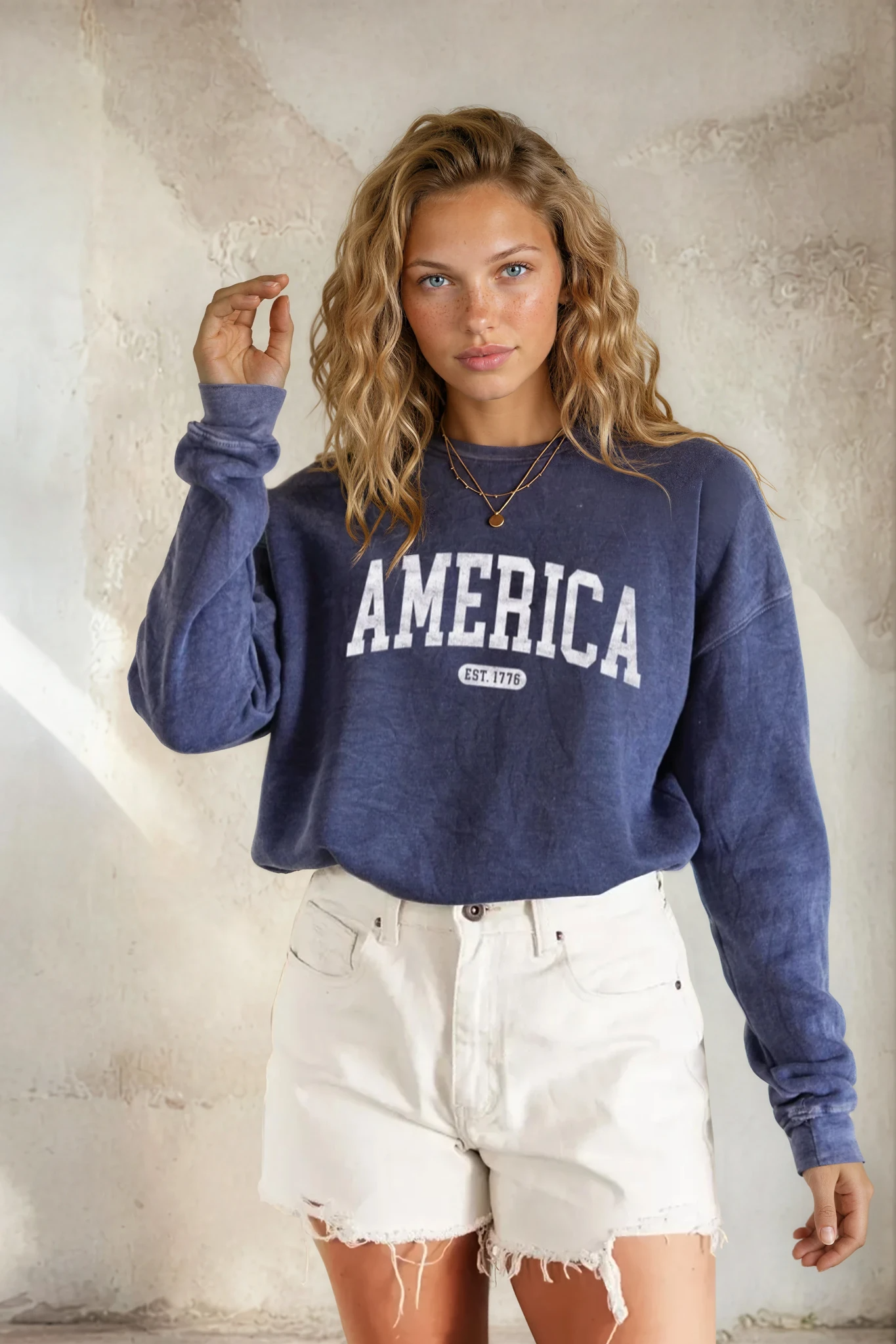 Woman wearing a blue 'AMERICA' sweatshirt against a textured wall.