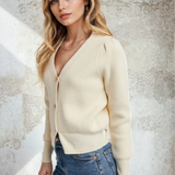 Woman wearing a cream cardigan and blue jeans against a textured wall.