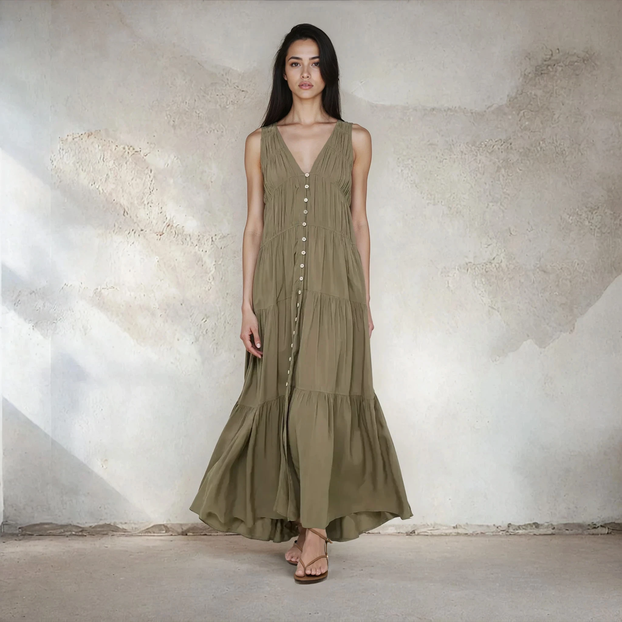 Woman wearing a long olive green dress against a textured white wall.