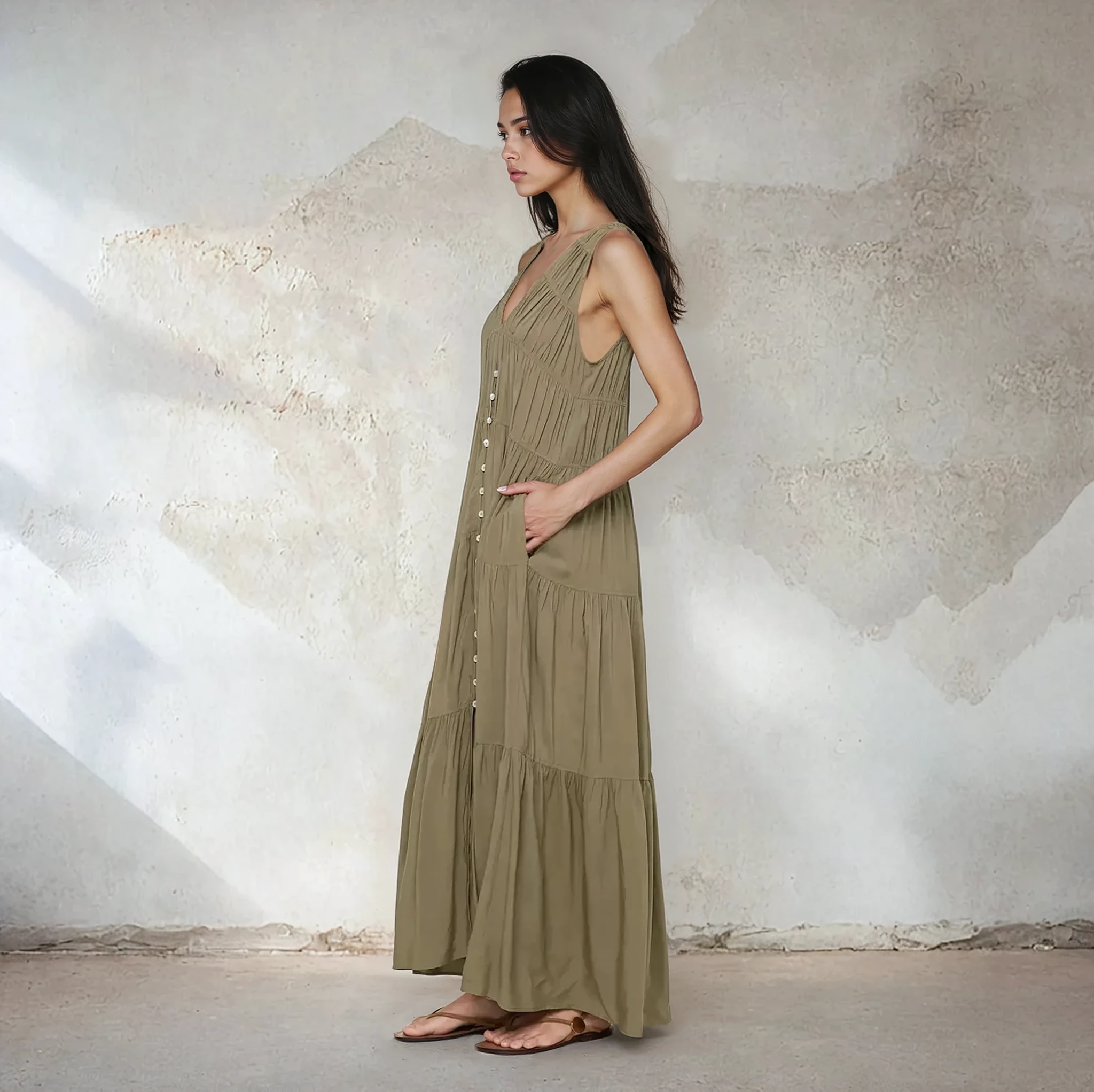 Woman wearing a long olive green dress against a textured wall.