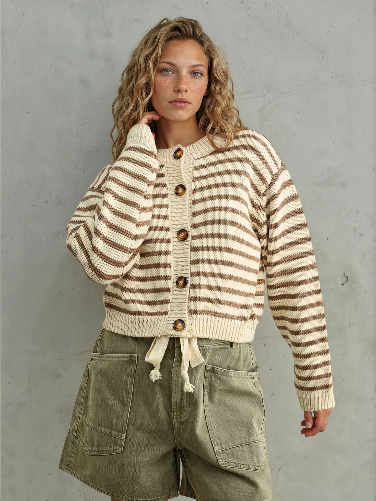 Woman wearing a striped cardigan and cargo shorts against a gray background