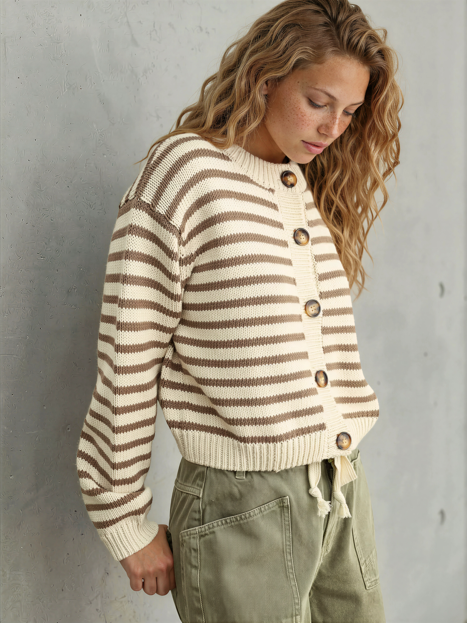 Woman wearing a striped sweater and cargo pants against a gray wall