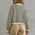 Person wearing a black and white striped sweater and beige pants against a gray concrete wall.