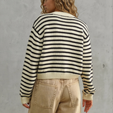 Person wearing a black and white striped sweater and beige pants against a gray concrete wall.