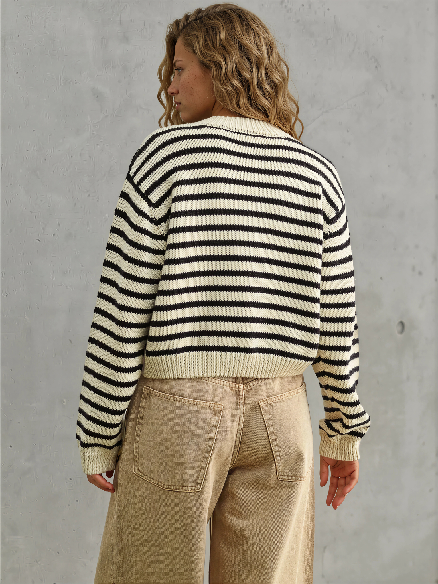 Person wearing a black and white striped sweater and beige pants against a gray concrete wall.