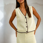 Woman wearing a cream-colored crochet outfit with black buttons against a light background