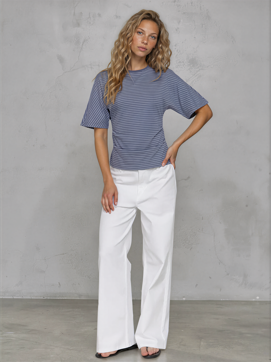 Woman wearing a blue striped shirt and white pants against a gray background