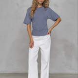 Woman wearing a blue striped shirt and white pants against a gray background