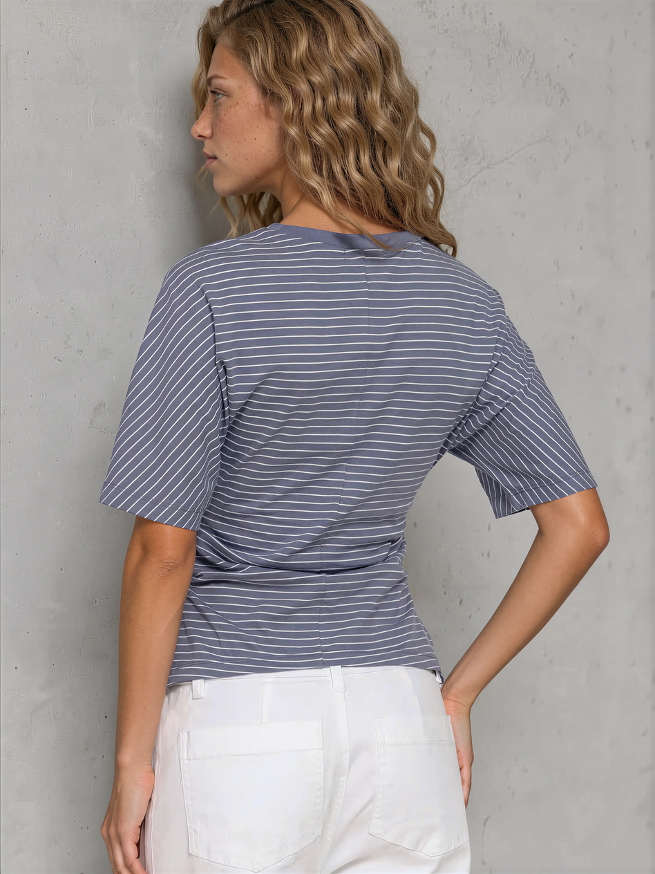 Woman wearing a blue striped shirt and white pants against a gray wall