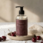 Hand soap bottle labeled 'Door County Cherry' by 'graced' on a wooden tray with cherries.
