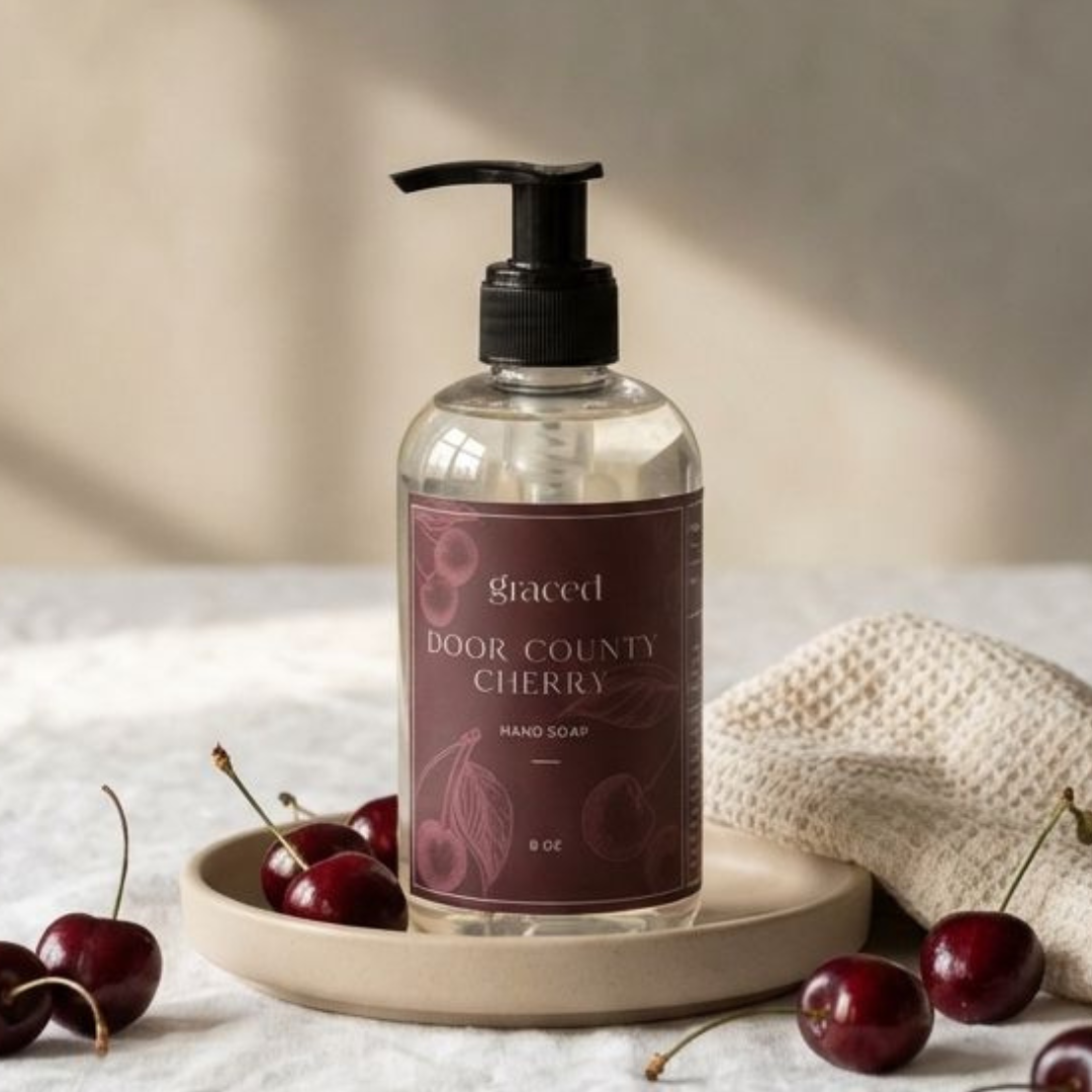 Hand soap bottle labeled 'Door County Cherry' by 'graced' on a wooden tray with cherries.