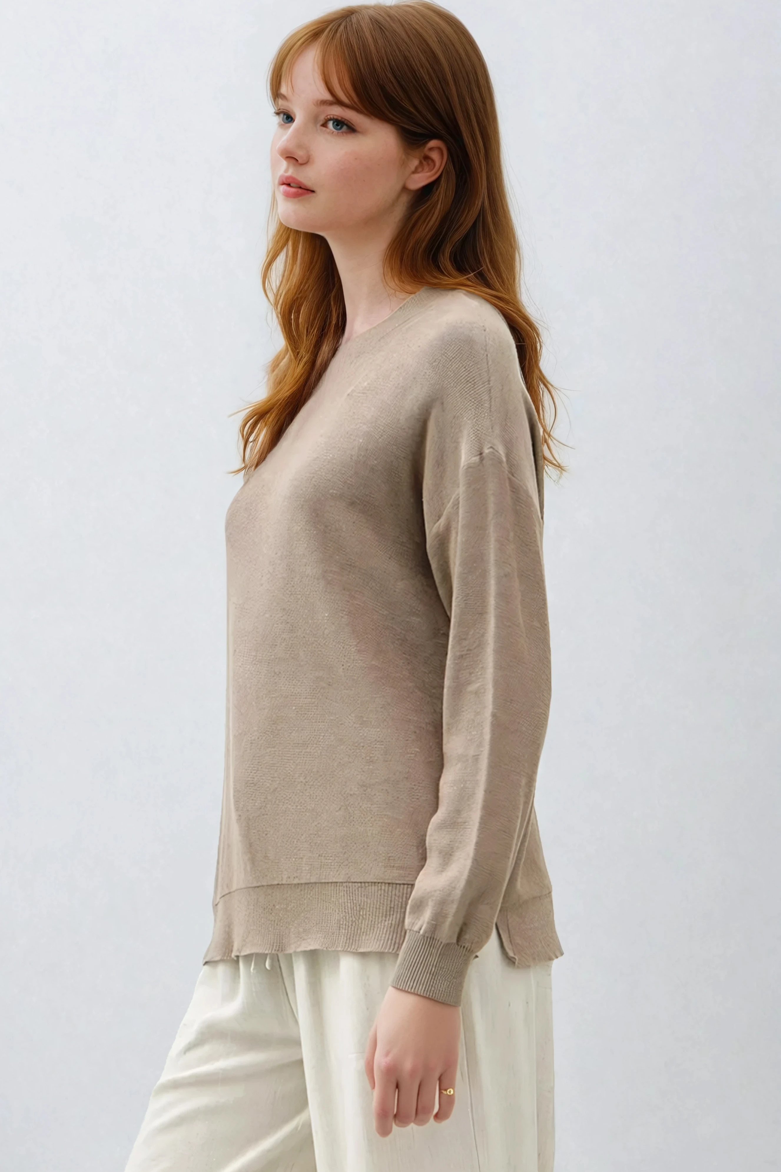 Woman wearing a beige sweater and white pants against a light gray background