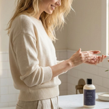 Woman applying soap to her hands in a bathroom setting with a bottle of soap on the counter.