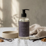 Hand soap bottle with a purple label on a textured surface with a towel and vanilla beans.