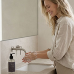 Woman washing hands with soap at a sink in a bathroom.