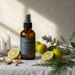 Bottle of 'Elevate' spray on a table with lemons, candles, and herbs