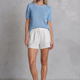 Woman wearing a blue sweater and white shorts against a gray concrete wall.