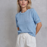 Woman wearing a light blue sweater and white shorts against a gray concrete wall.