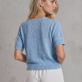 Woman wearing a blue knitted top and white shorts against a gray concrete wall.