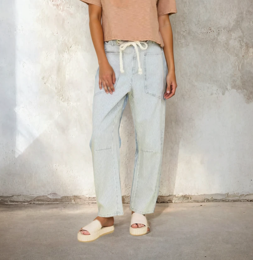 Person wearing light blue checkered pants and a beige top against a textured wall.