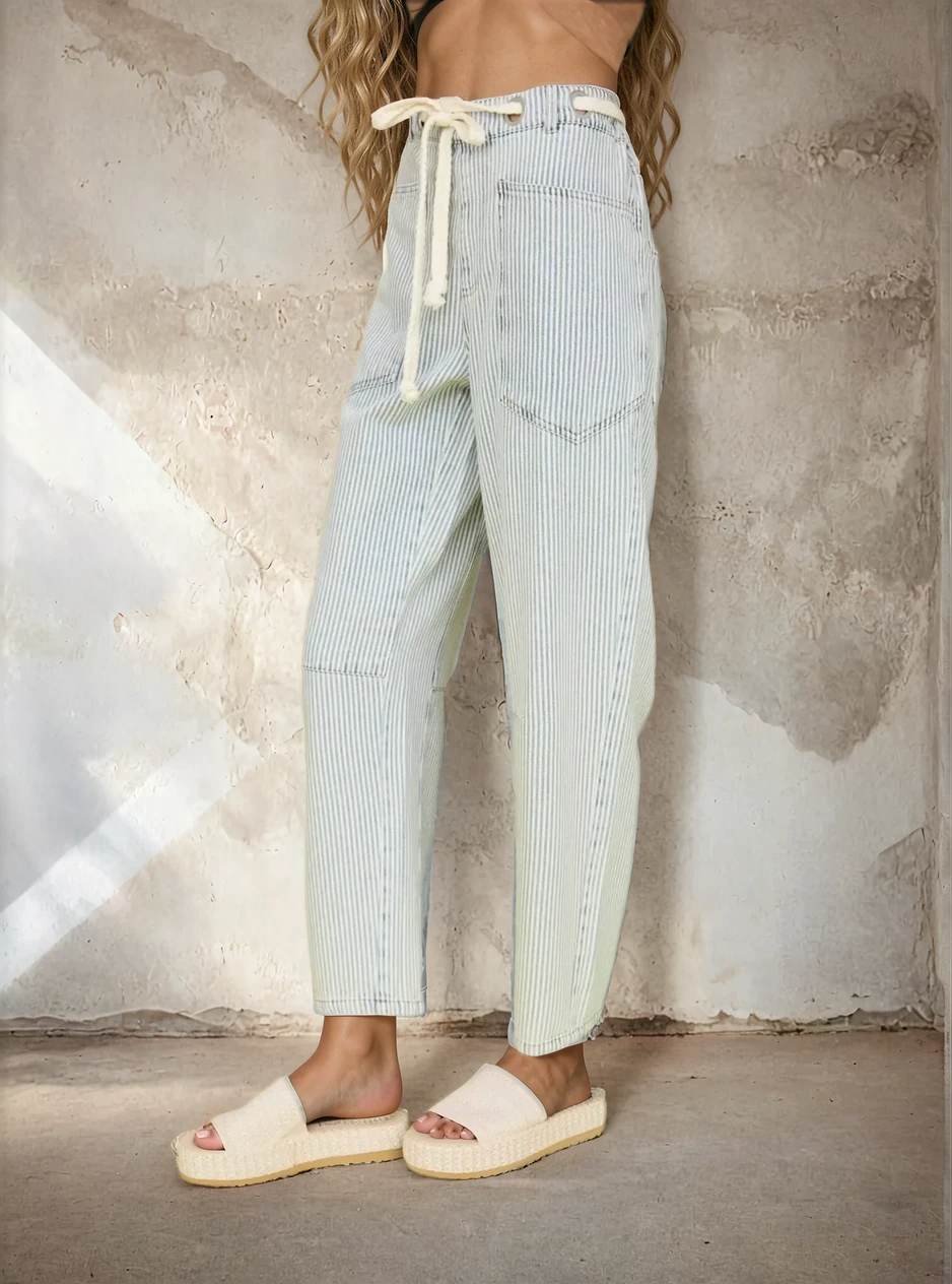 Person wearing light blue striped pants with a drawstring, standing against a textured wall.