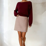 Woman wearing a burgundy sweater and beige skirt against a white background