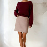 Woman wearing a burgundy sweater and beige skirt against a white background