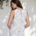 Woman wearing a light blue floral outfit against a white wall with greenery.