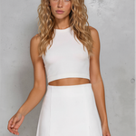 Woman wearing a white sleeveless top and skirt against a gray background
