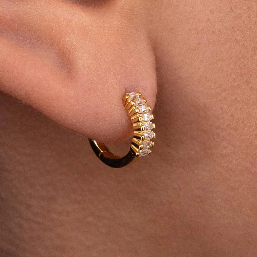 A close-up image of an 18K gold-plated stainless steel hoop earring with a secure lock mechanism, featuring a shiny finish and attached to an ear.