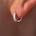 Silver hoop earring worn on a person's ear with a plain background