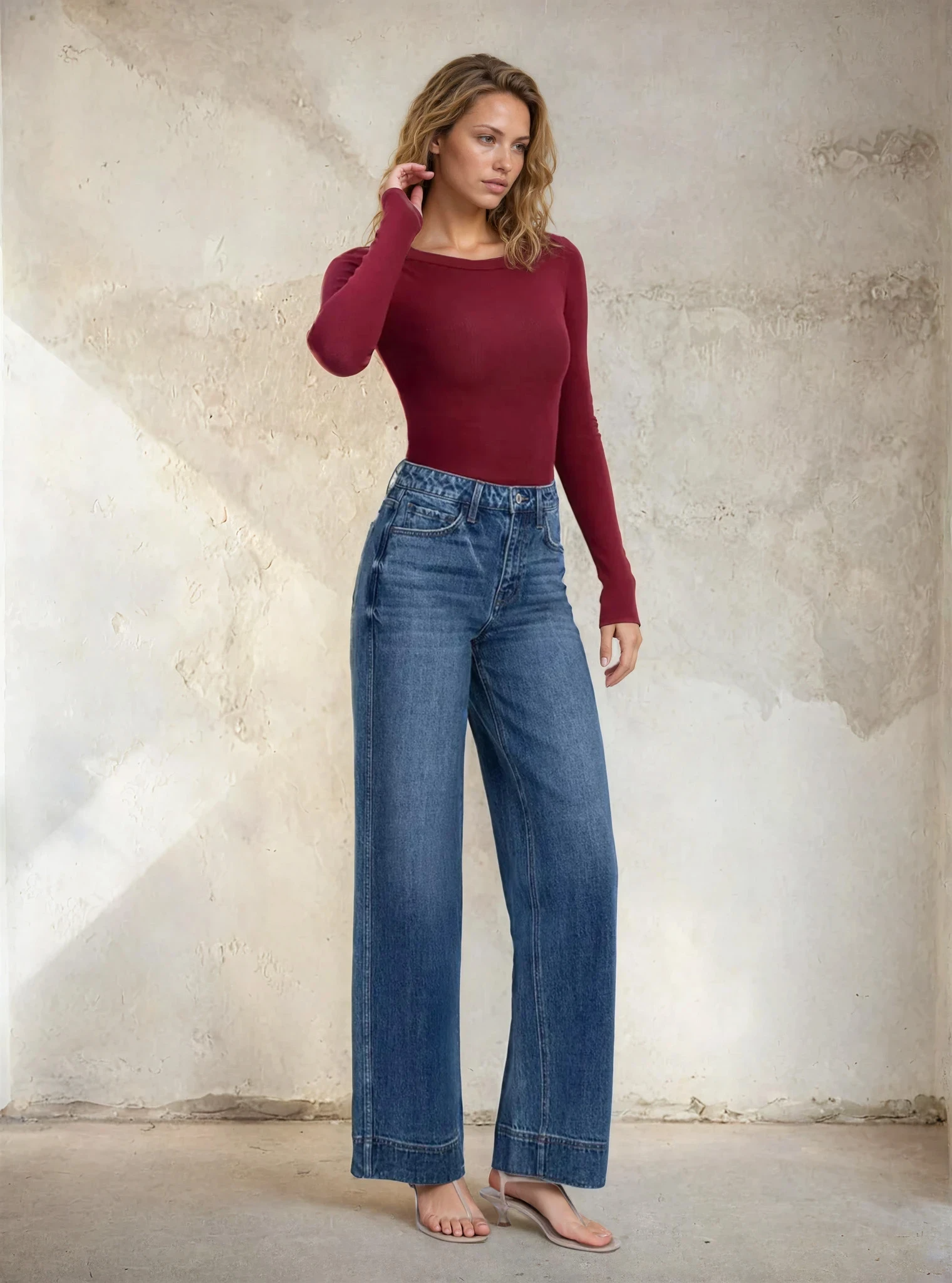 Woman wearing a red top and blue jeans against a textured wall.