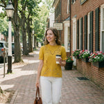 Woman walking down a street holding a coffee cup and a handbag
