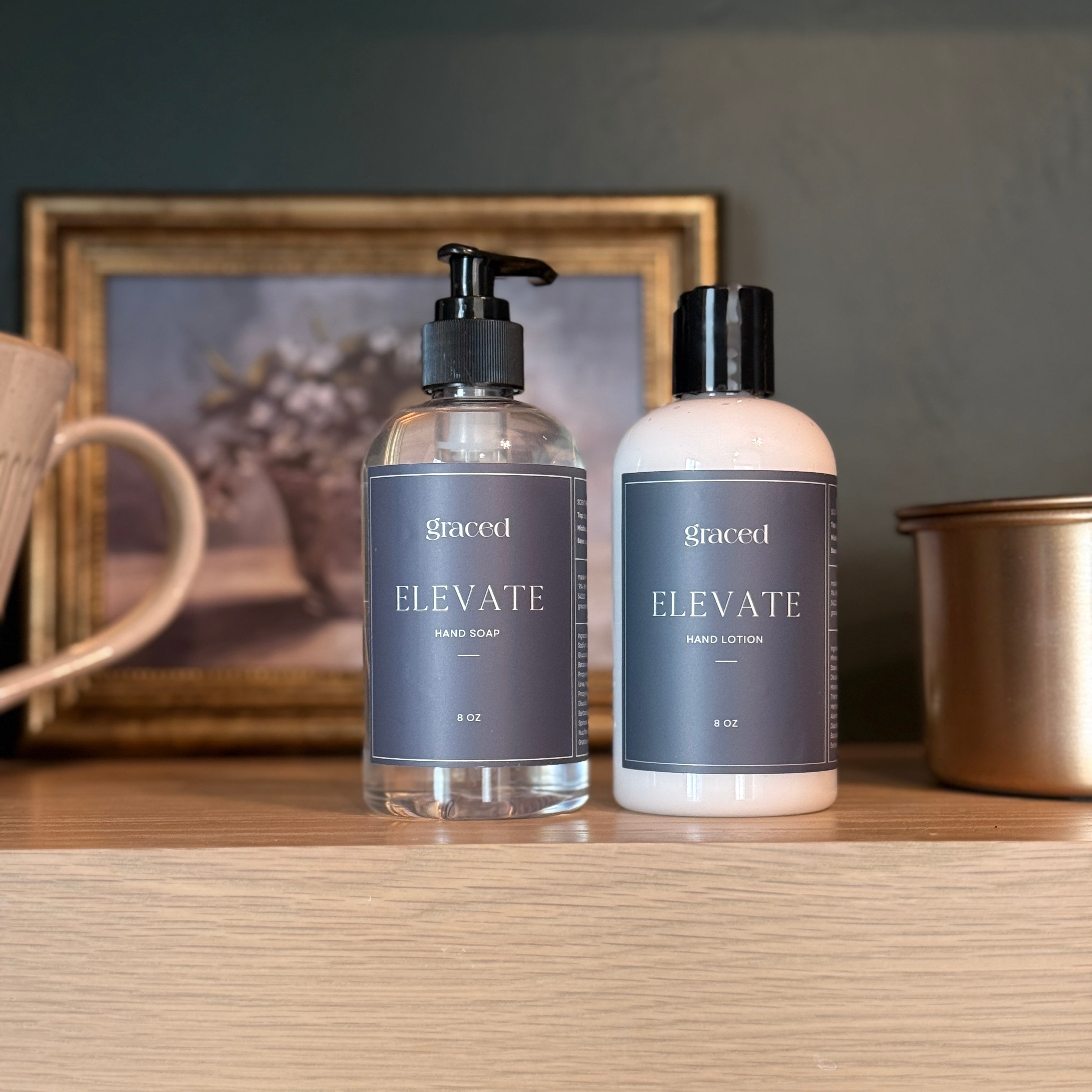Two bottles of 'Elevate' hand soap and lotion on a wooden surface with a decorative background.
