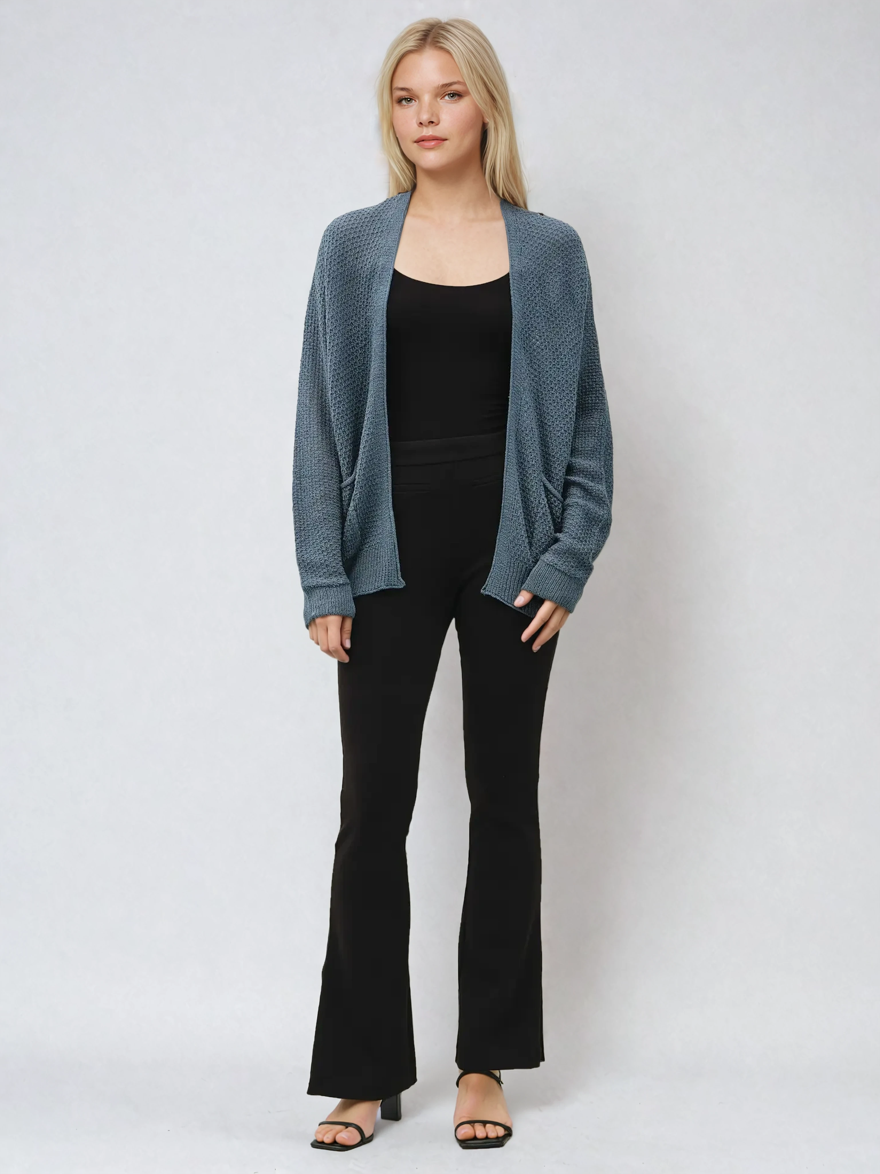Woman wearing a blue cardigan over a black top and pants on a white background