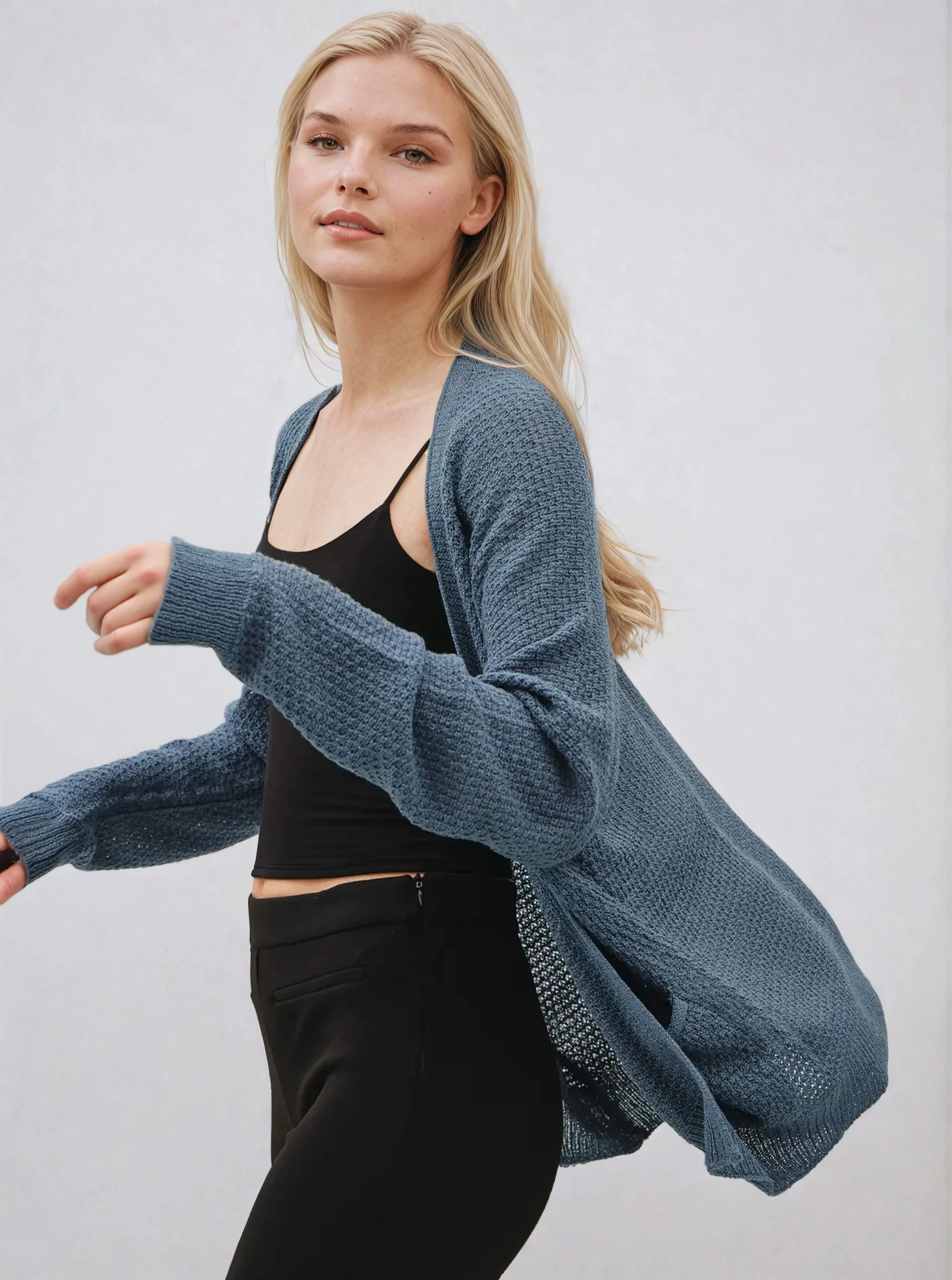 Woman wearing a blue cardigan over a black top and pants on a light gray background