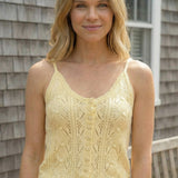 Woman wearing a yellow knitted tank top standing in front of a wooden house.