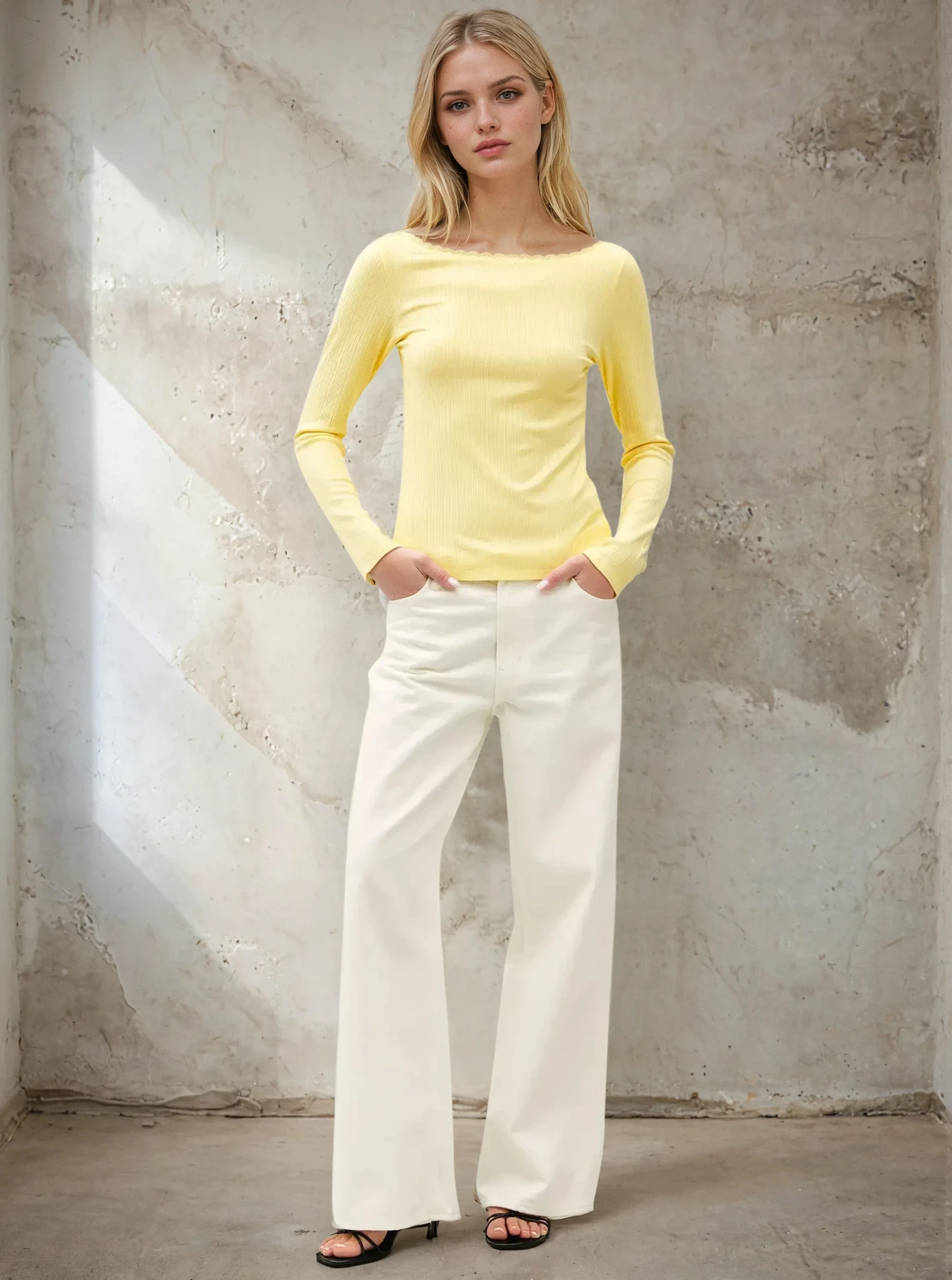 Woman wearing a yellow long-sleeve top and white pants against a textured wall.