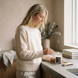 Woman in a kitchen lighting a candle on a countertop.
