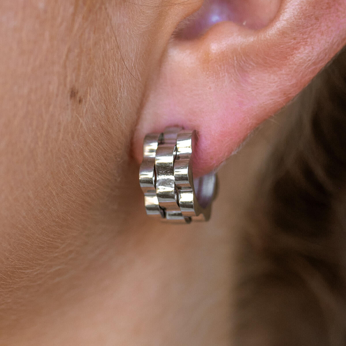A close-up image of a person wearing a silver hoop earring.