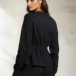 Woman wearing a black sweater against a textured white wall