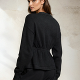 Woman wearing a black sweater against a textured white wall