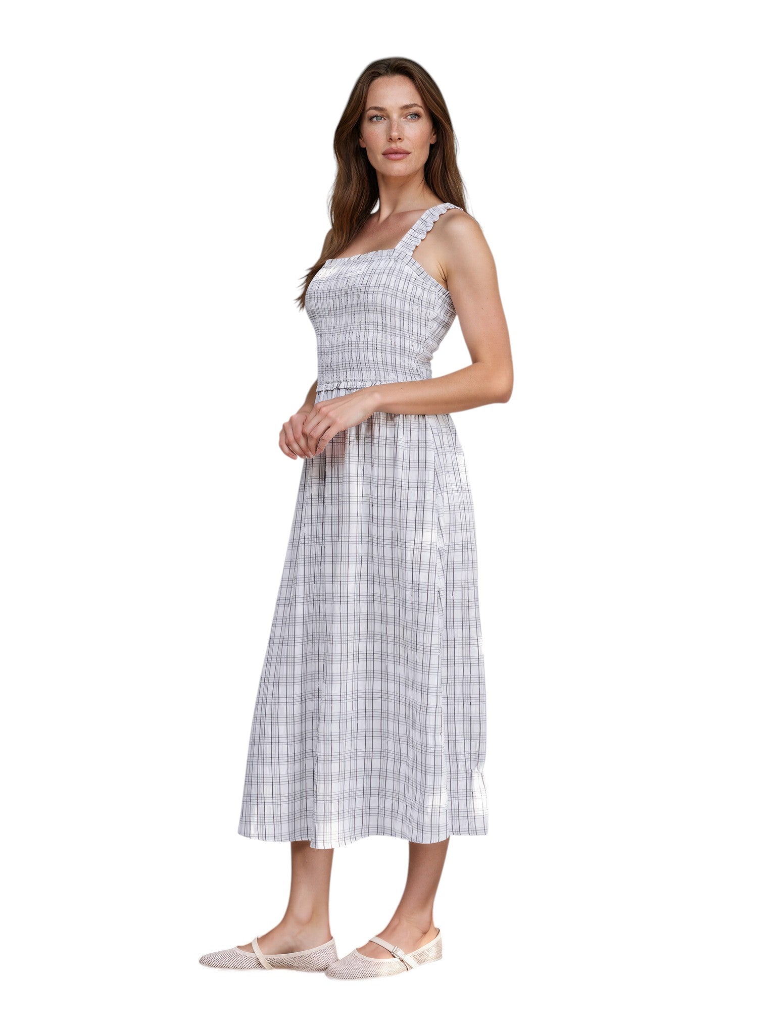 Woman in a checkered dress standing against a white wall with greenery.