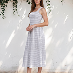 Woman in a checkered dress standing against a white wall with greenery.