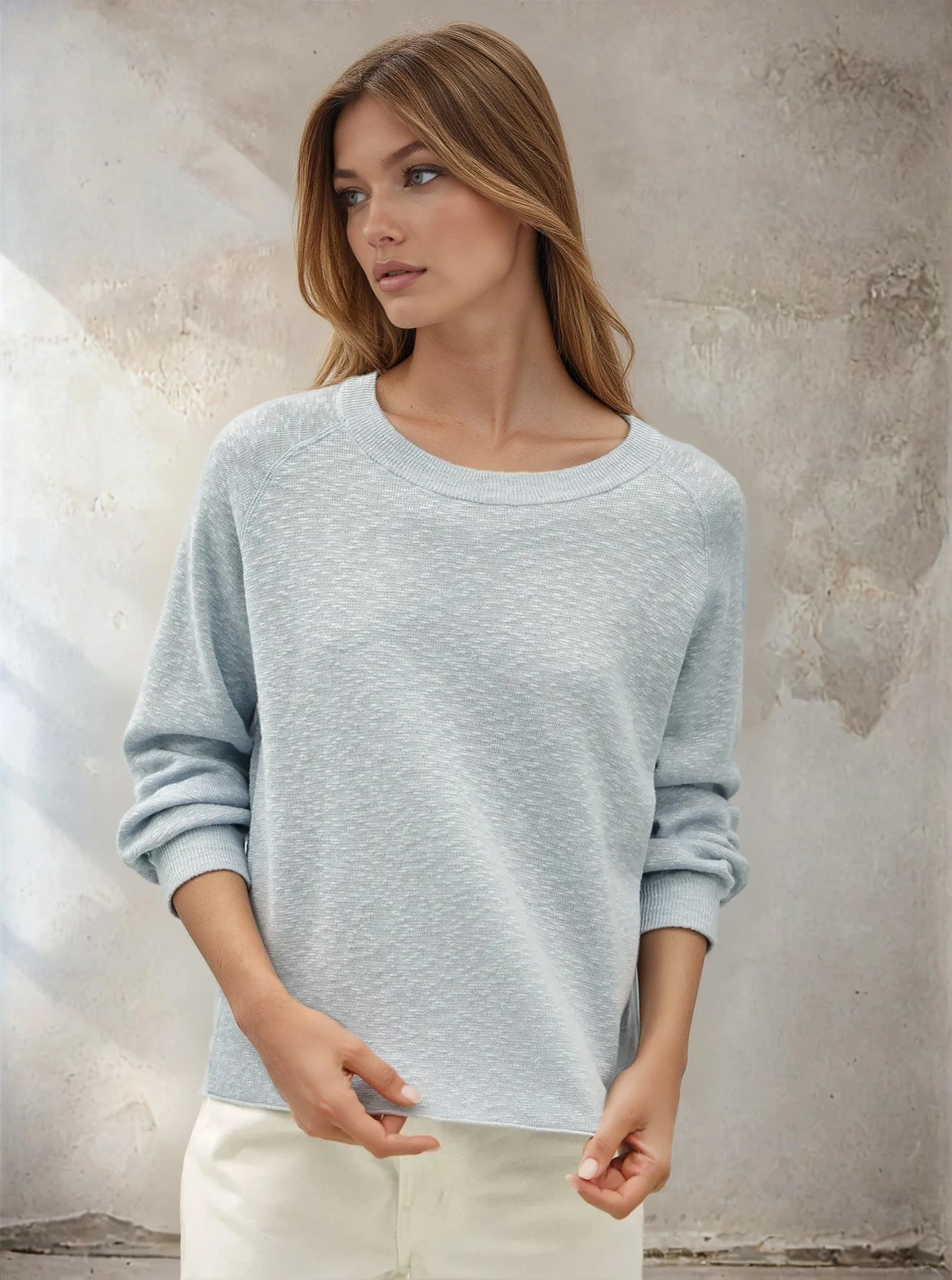 Woman wearing a light blue sweater against a textured wall.
